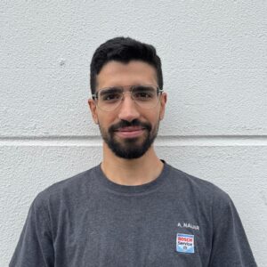 Eine lächelnde Person mit Brille und schwarzem Bart, trägt ein graues T-Shirt mit Bosch-Logo.